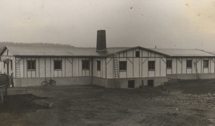 La photographie montre un bâtiment allongé percé de nombreuses fenêtres, dont l’allure évoque une maison à colombages.