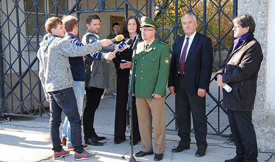 Press briefing in front of the Jourhaus. In the background is the gate with the missing postern. From left to right: members of the press, Dr Gabriele Hammermann, director of the Dachau Concentration Camp Memorial Site, police director Thomas Rauscher, head of the Dachau police branch, and Dr Ludwig Spaenle, Culture Minister. (Dachau Concentration Camp Memorial Site)