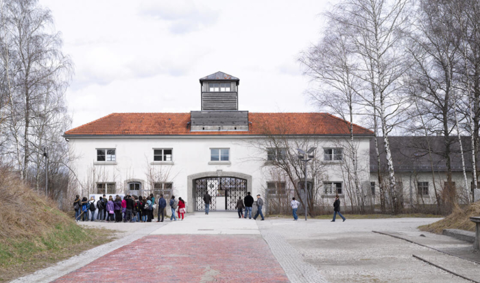 The Jourhaus is a building that has a long, elongated structure, with a small guard tower positioned in the middle on its roof. Underneath is a wide gateway; the iron gate has the inscription “Arbeit macht frei” (“work sets you free”).