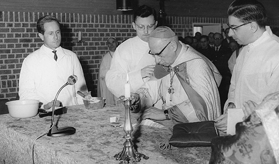 Johannes Neuhäusler in tunicle, flanked by three altar servers, in front of the altar of the convent church. Those attending the mass are crowded in the background. (archives Karmel Dachau)