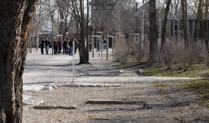 Kilka lekko wystających kamiennych fundamentów w żwirze, na drugim planie Centrum Informacyjne dla Zwiedzających i wieża wartownicza