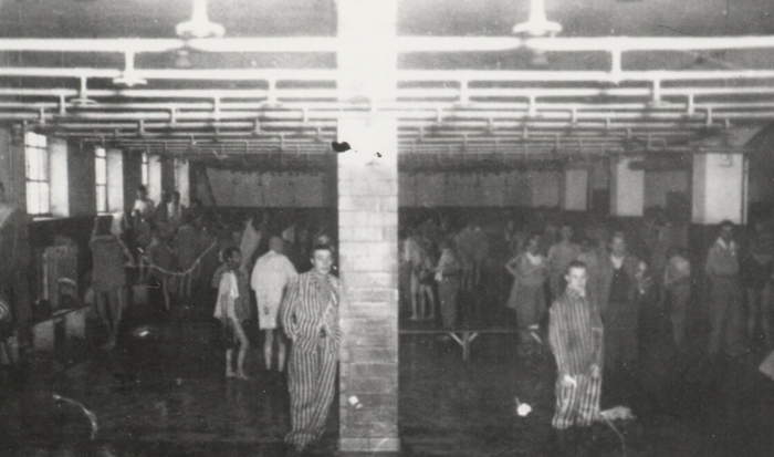 A group of liberated prisoners, some partly undressed, others still in the striped garb, stand under the showers in the prisoner baths.