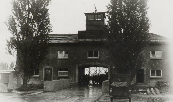 Viewed in the direction of the camp, the elongated Jourhaus stands behind two trees, a wide gateway running through the middle of the building. An iron gate with the inscription “Arbeit macht frei” (“work sets you free”) served as the camp’s entrance and exit. Today it is still the main access for visitors to the Memorial Site.