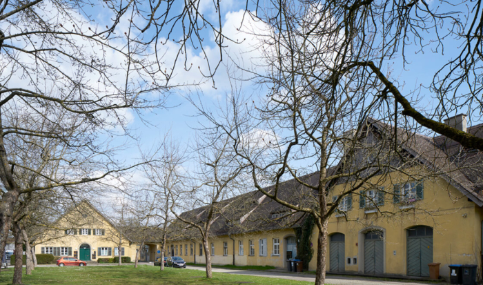 Derrière des arbres, on aperçoit une bâtisse de forme allongée, au crépi jaune, qui abritait l’administration et l’institut de l’ancien « jardin médicinal ». Son allure rappelle un bâtiment agricole.