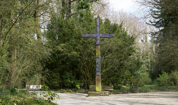 Surrounded by trees and bushes, a large cross was erected on a gravel path.