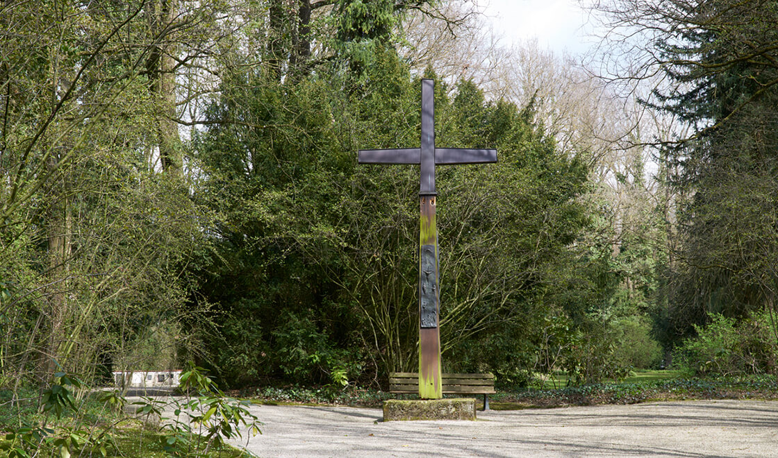 Umringt von Bäumen und Büschen wurde auf einem Kiesweg ein großes Kreuz aufgestellt.