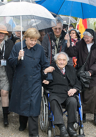 Kanclerz dr Angela Merkel idzie obok ocalałego byłego więźnia Maxa Mannheimera, który porusza się na wózku inwalidzkim. Max Mannheimer trzyma ją pod rękę. (Sebastian Freller)