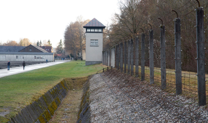 Les installations de surveillance ont été reconstruites. Le site du camp est d’abord bordé d’une pelouse. À droite se trouve un fossé de deux mètres de profondeur entouré d’un obstacle en fil de fer barbelé. Une clôture de barbelés électrifiés figure sur le bord droit de la photo et au loin, on distingue un mirador carré, lui aussi reconstruit.