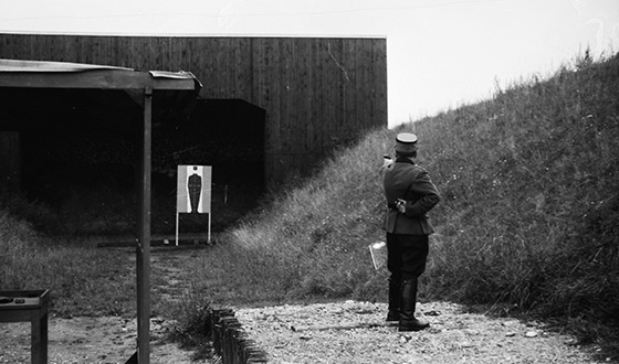 Esesman z wyciągniętą ręką, w której trzyma pistolet, celuje do tarczy w kształcie człowieka (Heinz Bielmeier, Dachau)