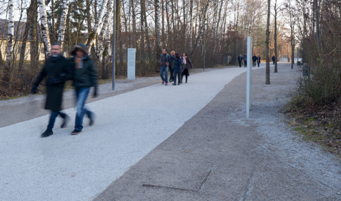 Zwei parallel angeordnete Metallwinkel, die neben dem befestigtes Fußweg leicht erhoben sind und den ehemaligen Standort der Politischen Abteilung anzeigen.