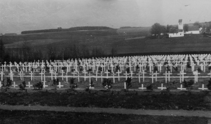 De nombreuses croix blanches se dressent en rangées parallèles dans le champ funéraire du cimetière Waldfriedhof. Au loin, on aperçoit une église.