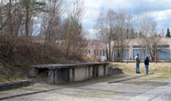 Vorne im Bild: Die linke Seite von der Verbindungs·straße zum SS-Lager. Hinten: Die ehemalige Lager·bäckerei. Das Foto ist von 2017.