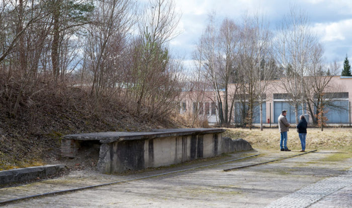 Made of demolition material, an embankment wall with trees adjoins the remnants of a rail track. This is located on the left side of the former connecting road to the SS camp. The former camp bakery is in the background.