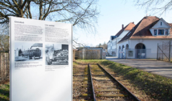 Links: Informations·tafel 4 vom Weg des Erinnerns Mitte: Gleis·stück an der Isar-Amperwerke-Straße Das Foto ist von 2017. (KZ-Gedenk·stätte Dachau)