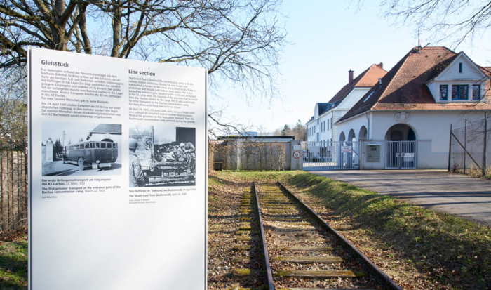 In der Mitte des Bildes ist ein Gleisstück zu sehen, das zum ehemaligen SS-Gelände führt. Im Vordergrund ist eine Tafel des “Weg des Erinnerns” angebracht, die Aufschluss über die Nutzung dieses noch erhaltenen Gleisstückes gibt .