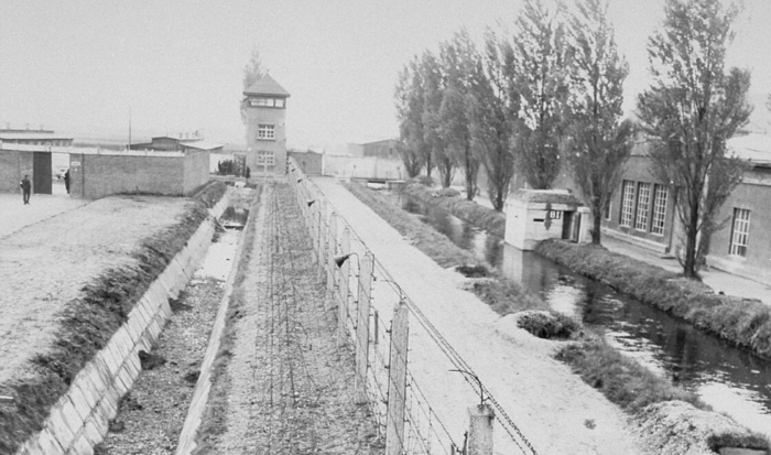 In der Ferne lässt sich ein Wachturm erkennen, vor dem sich die unüberwindbare Bewachungsanlage befindet. Rechts neben der Rasenfläche, die an das Lagergelände anschließt, befindet sich ein zwei Meter tiefer Graben, der in ein Stacheldrahthindernis übergeht. Der Stacheldrahtzaun bildet das letzte Hindernis der sehr sicher konstruierten Anlage. Rechts neben dem Zaun geht ein Weg an einem kleinen Fluss, der Würm entlang, an dessen Ufer Gebäude des SS-Geländes zu erkennen sind.