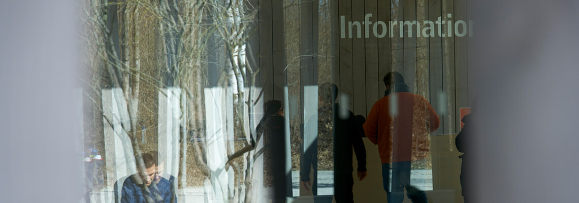 Photographie de la façade du centre d’accueil, à travers laquelle on aperçoit le reflet d’un visiteur devant le point d’information