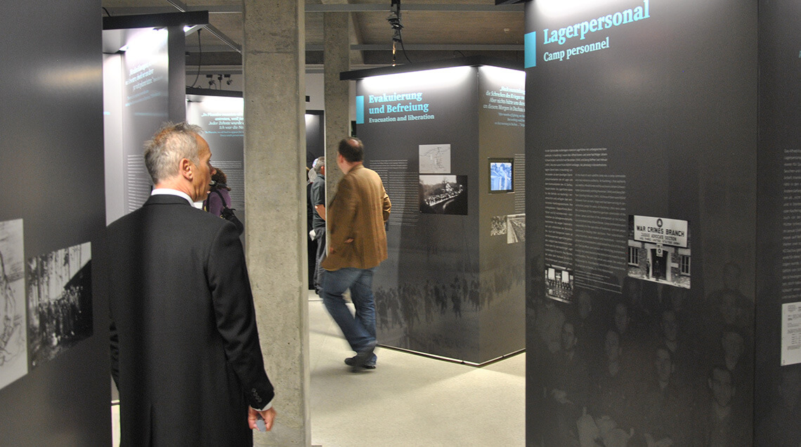 Mehrere Besucher laufen durch die Ausstellung „Sie gaben uns wieder Hoffnung”. Es sind einige graue Schautafeln aufgestellt, an denen Texte und Bilder zu sehen sind.