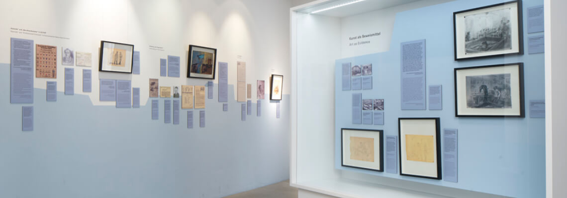 Blick auf eine Vitrine und eine Wand mit Bildern und Zeichnungen des Dachau-Überlebenden Georg Tauber