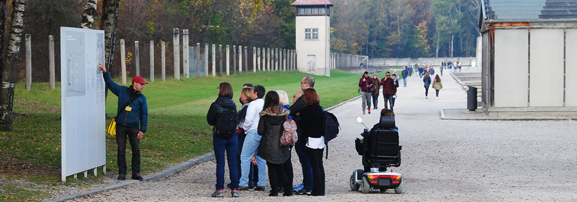 Besucherinnen und Besucher bei einem geführten Rundgang. Einer der Besucher ist im Rollstuhl unterwegs.