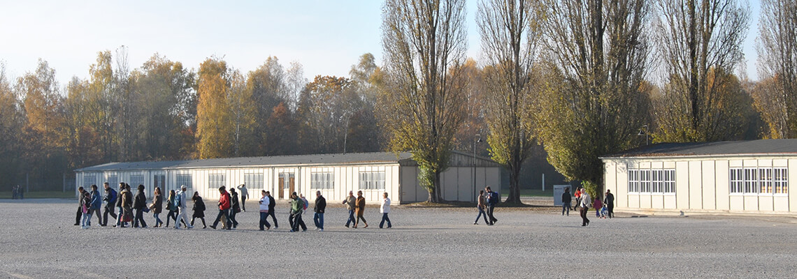 Besucherinnen und Besucher bei einem geführten Rundgang vor einer der rekonstruierten Modellbaracken