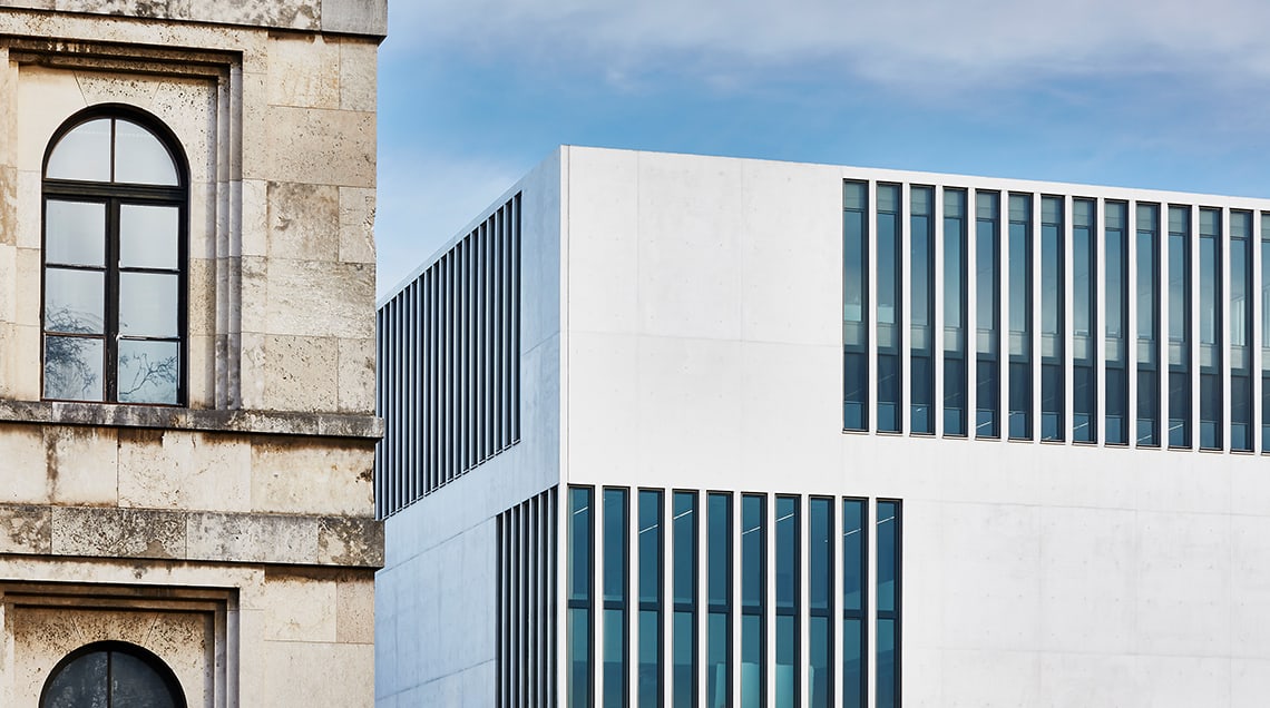 Einem Fassadendetail des NS-Dokumentationszentrums München steht auf dem Foto die Teilansicht des benachbarten ehemaligen „Führerbaus“ gegenüber.