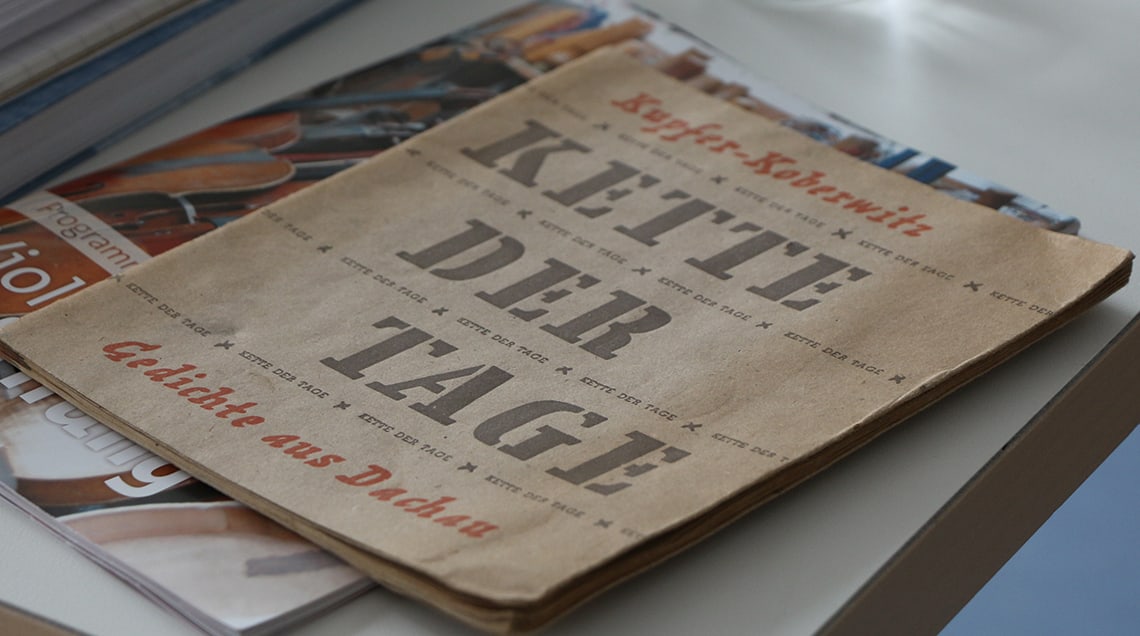 Arbeitstisch mit verschiedenen Büchern und Heften. Obenauf liegt das Heft “Kette der Tage” mit den Gedichten von Edgar Kupfer-Koberwitz, der das KZ Dachau überlebte