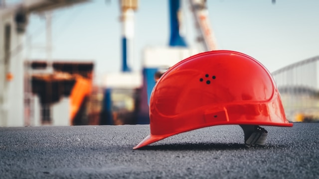 Ein roter Schutzhelm liegt auf dem Gehsteig vor einer Baustelle