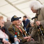 Zwei ältere Personen, eine sitzend, begrüßen sich und lächeln sich an