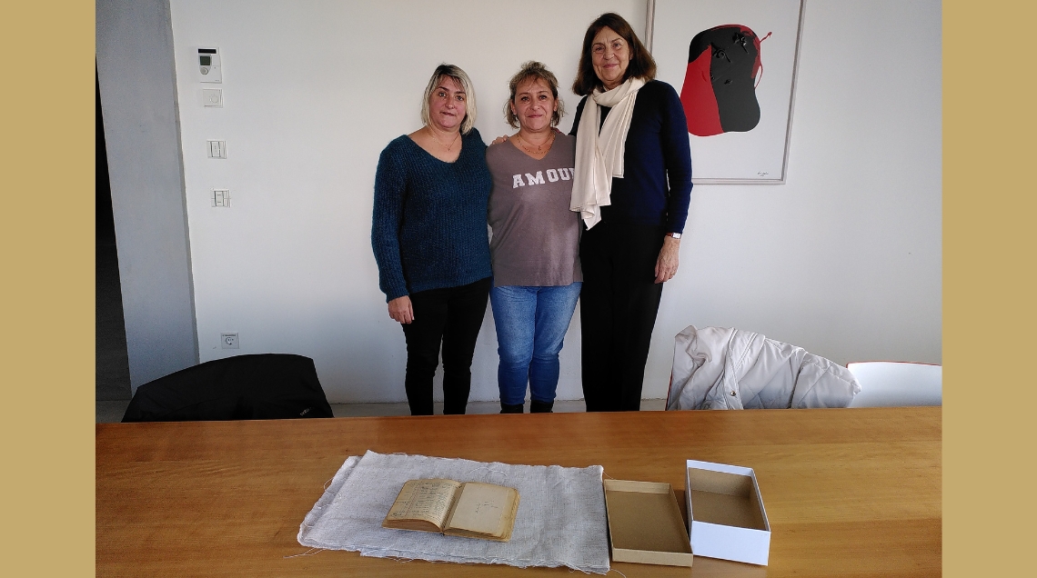 Drei Frauen stehen vor einem Tisch, auf dem ein erkennbar altes Buch auf einem Tuch ausgebreitet liegt